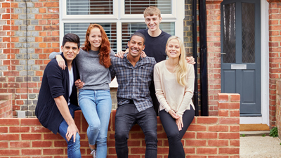 group of diverse young adults outside shared house smiling